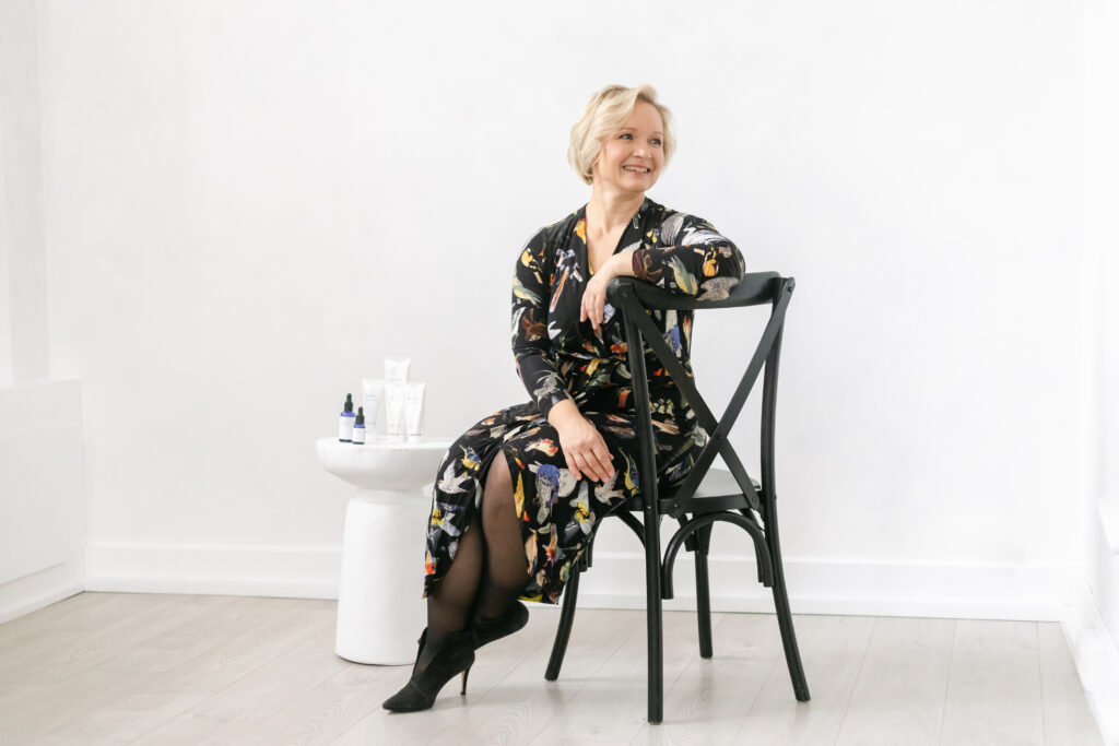 Facialist seated in a bright skincare studio beside treatment products